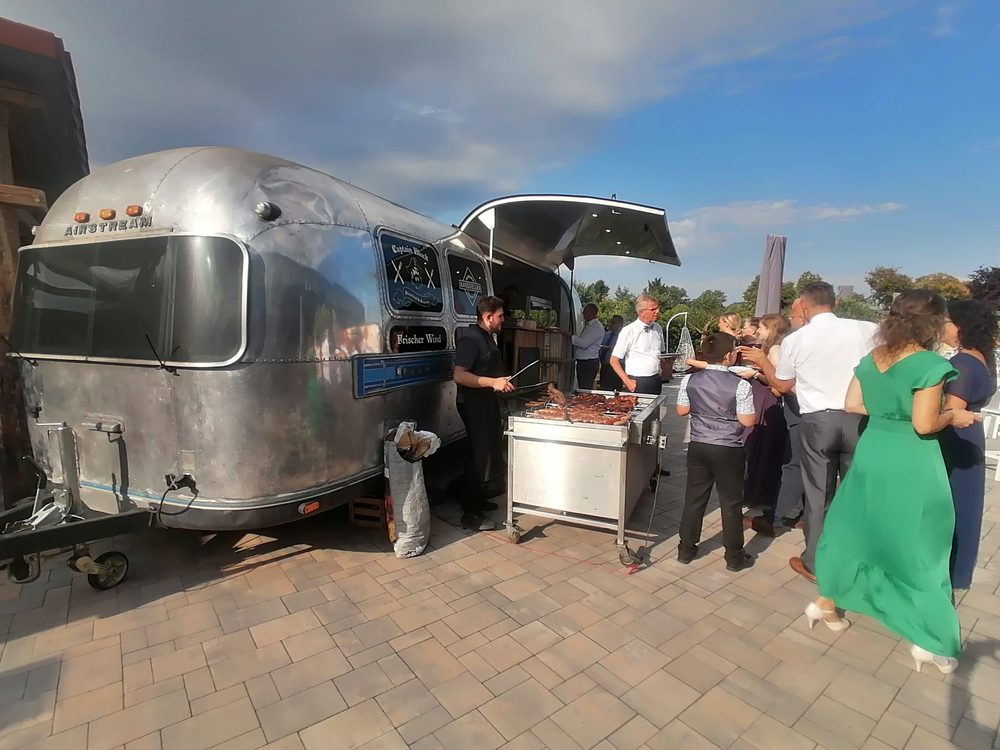 Captain Blocks Streetfood – Airstream Food Trailer (Baujahr 1978) im Catering-Einsatz bei einer Hochzeit, mit Grillstation für Rebknorzespieße und Bratwurst